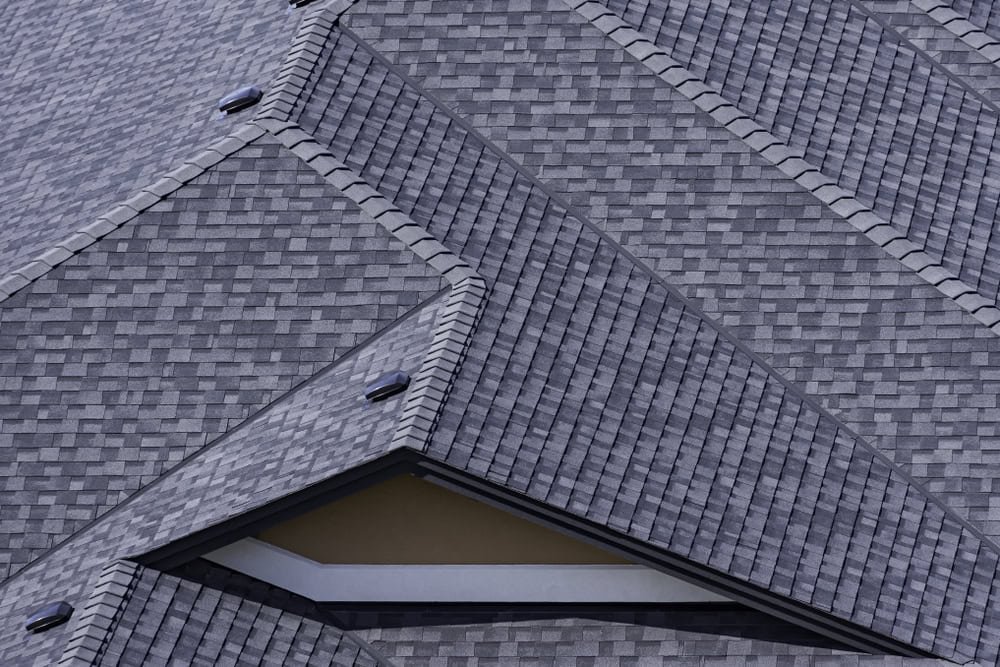 Close-up of a rooftop with overlapping, textured gray asphalt shingles arranged in a geometric pattern, showcasing varying angles and slopes.