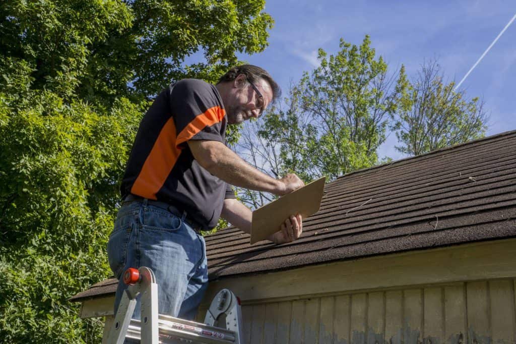 A man on a ladder checking the roof of a house.