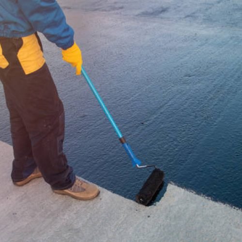 Roofer worker painting black coal tar or bitumen at concrete surface by the roller brush, A waterproofing. industrial worker on construction site laying sealant for waterproofing cement