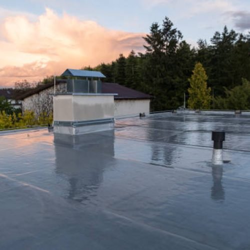 Flat roof covered with bitumen membrane and silver lacquer with chimney on a private house. Reflections after rain