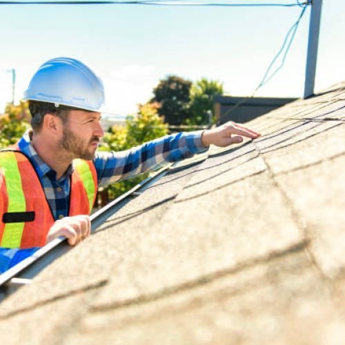 A man with hard hat standing on steps inspecting house roof