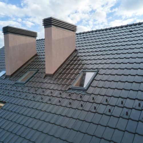 Closeup of attic windows and brick chimneys on house roof top covered with ceramic shingles. Tiled covering of building.