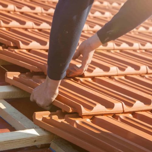 AKM 941 Roofing crew member installing shingles on a pitched roof in Lee County, FL, using safety harnesses and tools, with a focus on durability and professional workmanship under sunny skies.
