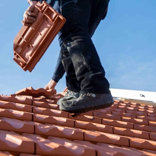 Roofing technician from AKM 941 Roofing installing shingles on a residential roof in Lee County, FL, demonstrating precision and safety with professional-grade equipment under bright daylight.
