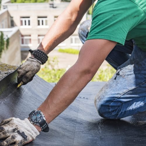 A construction worker cuts waterproofing material and prepares it for installation. Overhaul of the roof of the house.